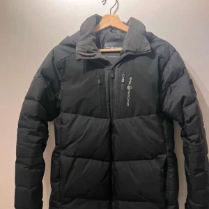 Sail Racing jacka - Säljer en svart dunjacka från Sail Racing i mycket bra skick. Jackan har en dragkedja framtill och en bröstficka med dragkedja. Perfekt för kalla vinterdagar med sin quiltade design som håller värmen. Den är långärmad och har en stilren look. Hör av er vid mer frågor!!!