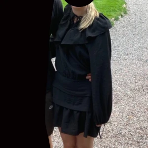 Svart klänning med volangdetaljer - Snygg svart klänning med volangdetaljer och långa ärmar. Perfekt för höst och vinter. Klänningen har en normal passform och är tillverkad i ett mjukt material som ger en bekväm känsla.