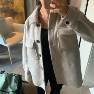 Beige overshirt från Dobber - Säljer en superfin beige overshirt från Dobber i storlek XS. Den har långa ärmar och knappar framtill, samt ett bälte i midjan för en snygg passform. 