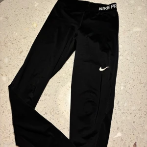 Svarta Nike Pro leggings - Säljer ett par svarta Nike Pro leggings i storlek S. De är tillverkade i Dri-FIT-material som håller dig torr och bekväm under träning. Perfekta för gymmet eller löprundan! De har en tight passform och Nike-loggan på benet.
