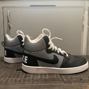 Svartvita Nike sneakers - Snygga svartvita Nike sneakers med ett coolt rutigt mönster på sidorna. De har en hög modell med snörning och en stor Nike-logga på hälen. Perfekta för vintern. Skorna ser ut att vara i bra skick och har endast använts cirka 2 gånger.