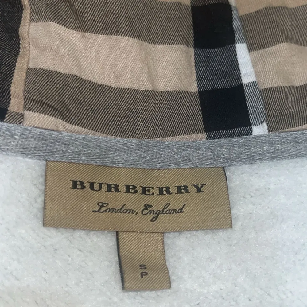 Säljer en snygg grå hoodie från Burberry i mycket bra skick. Den har en klassisk dragkedja och en huva med det ikoniska Burberry-mönstret på insidan. Perfekt för både höst och vår. Passar till alla tillfällen när du vill vara både bekväm och stilren. Storlek S passar M.. Tröjor & Koftor.