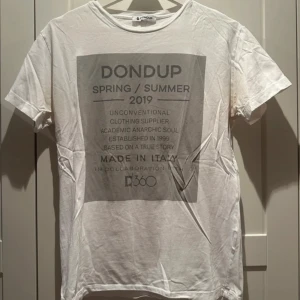 Vit t-shirt från Dondup - Säljer en vit t-shirt från Dondup med tryck på framsidan. Den är från deras vår/sommar 2019-kollektion och har en avslappnad stil. Perfekt för en casual look eller sommarhäng. Tillverkad i Italien och i bra skick.