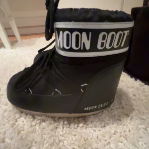 Moon Boots - Säljer ett par svarta Moon Boots i mycket bra skick. De är perfekta för vintern med sin varma och vadderade insida. Skorna har snörning och en cool design med loggan runt skaftet. Perfekta för att hålla fötterna varma och stiliga i snön!