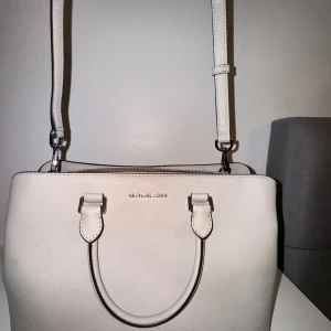 Beige handväska från Michael Kors - Snygg beige handväska från Michael Kors i mycket bra skick. Väskan har en stilren design med dragkedja och justerbar axelrem. Perfekt för både vardag och fest! 👜✨