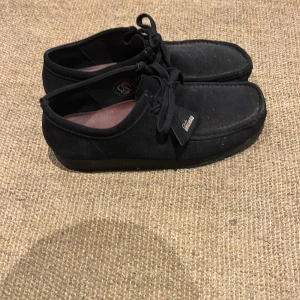 Svarta mockaskor från Clarks - Säljer ett par snygga svarta mockaskor från Clarks i bra skick. De har en klassisk design med snörning och en bekväm sula. Perfekta för både vardag och lite finare tillfällen. Skorna är i storlek herr 44.