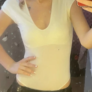 Vit kortärmad bodysuit - Säljer en stilren vit bodysuit med korta ärmar och v-ringning. Perfekt för sommardagar eller som basplagg under en kavaj. Materialet är mjukt och stretchigt för en bekväm passform. Passar till både vardag och fest!