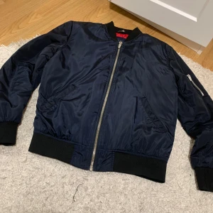 Mörkblå bomberjacka från Zara Man - Säljer en snygg mörkblå bomberjacka från Zara Man i storlek M. Jackan har en dragkedja framtill och en cool röd quiltad insida. Perfekt för höst och vår!