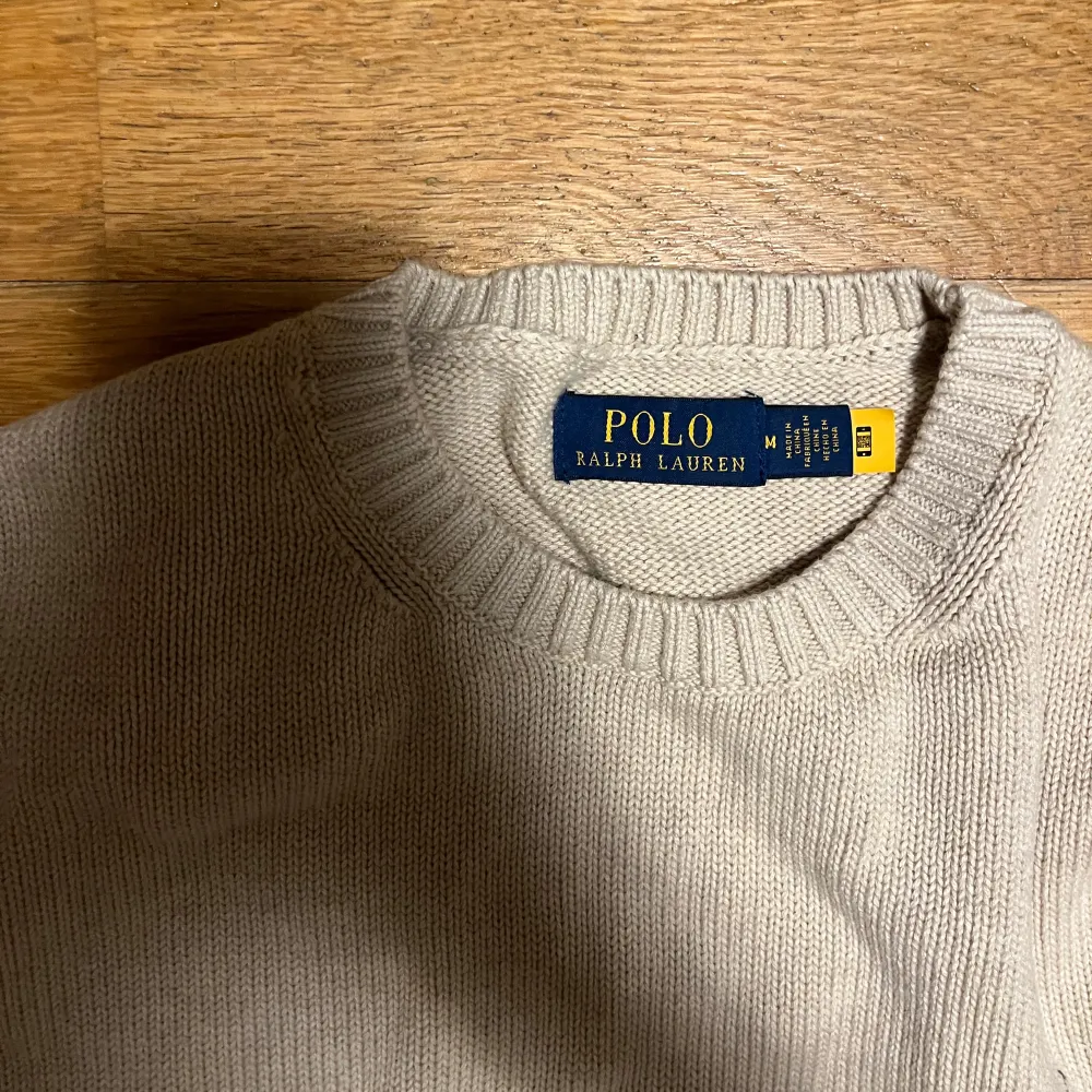 Säljer en stilren beige tröja från Polo Ralph Lauren i storlek M. Den är stickad och har en klassisk rund halsringning. Tröjan har långa ärmar och den ikoniska loggan broderad på bröstet. Perfekt för både höst och vår!. Tröjor & Koftor.