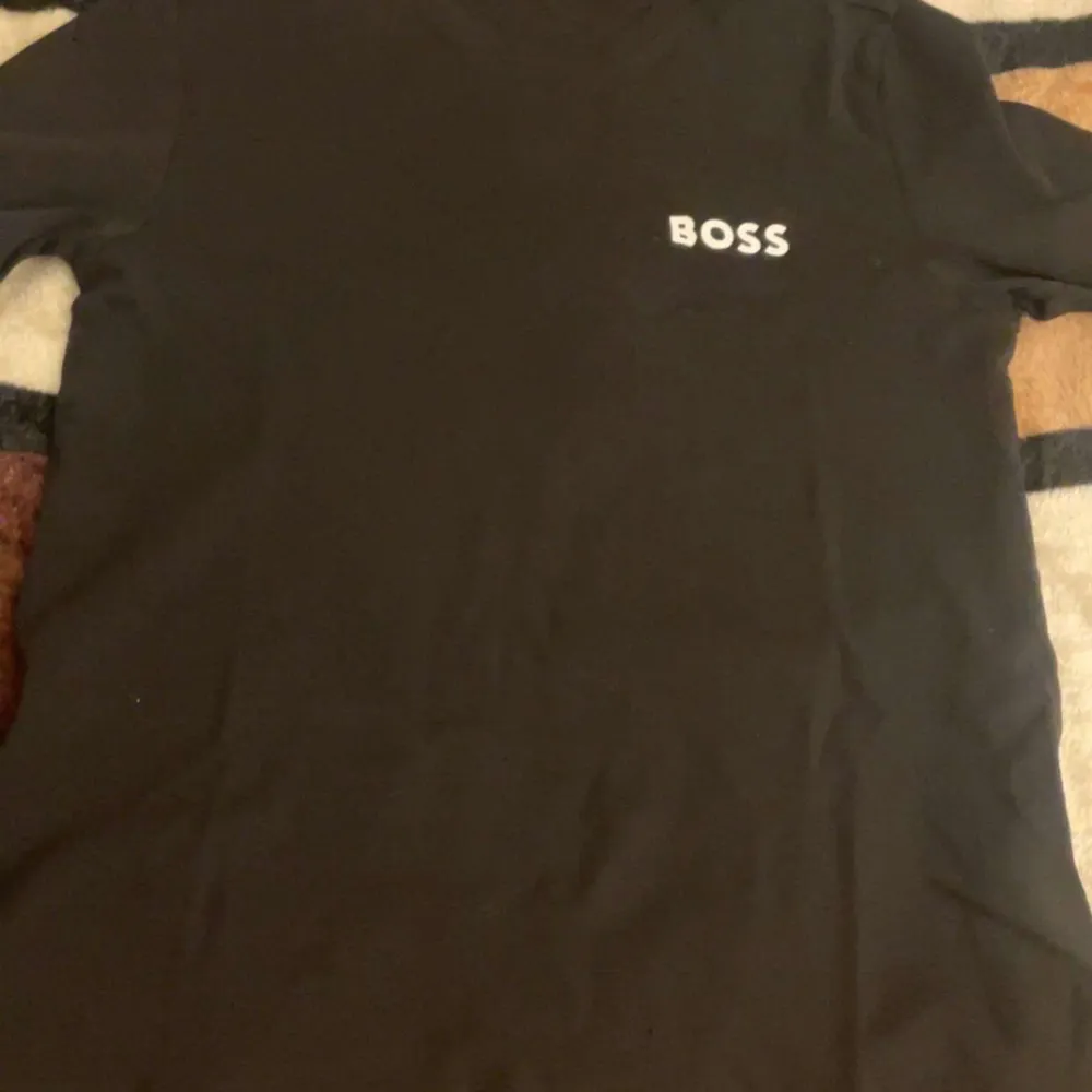 Säljer en stilren svart t-shirt från BOSS i storlek M. Den har en enkel design med BOSS-loggan tryckt på bröstet. Perfekt för en casual look eller att klä upp med en snygg jacka. T-shirten är i bra skick och gjord av mjukt material för en bekväm passform.. T-shirts.