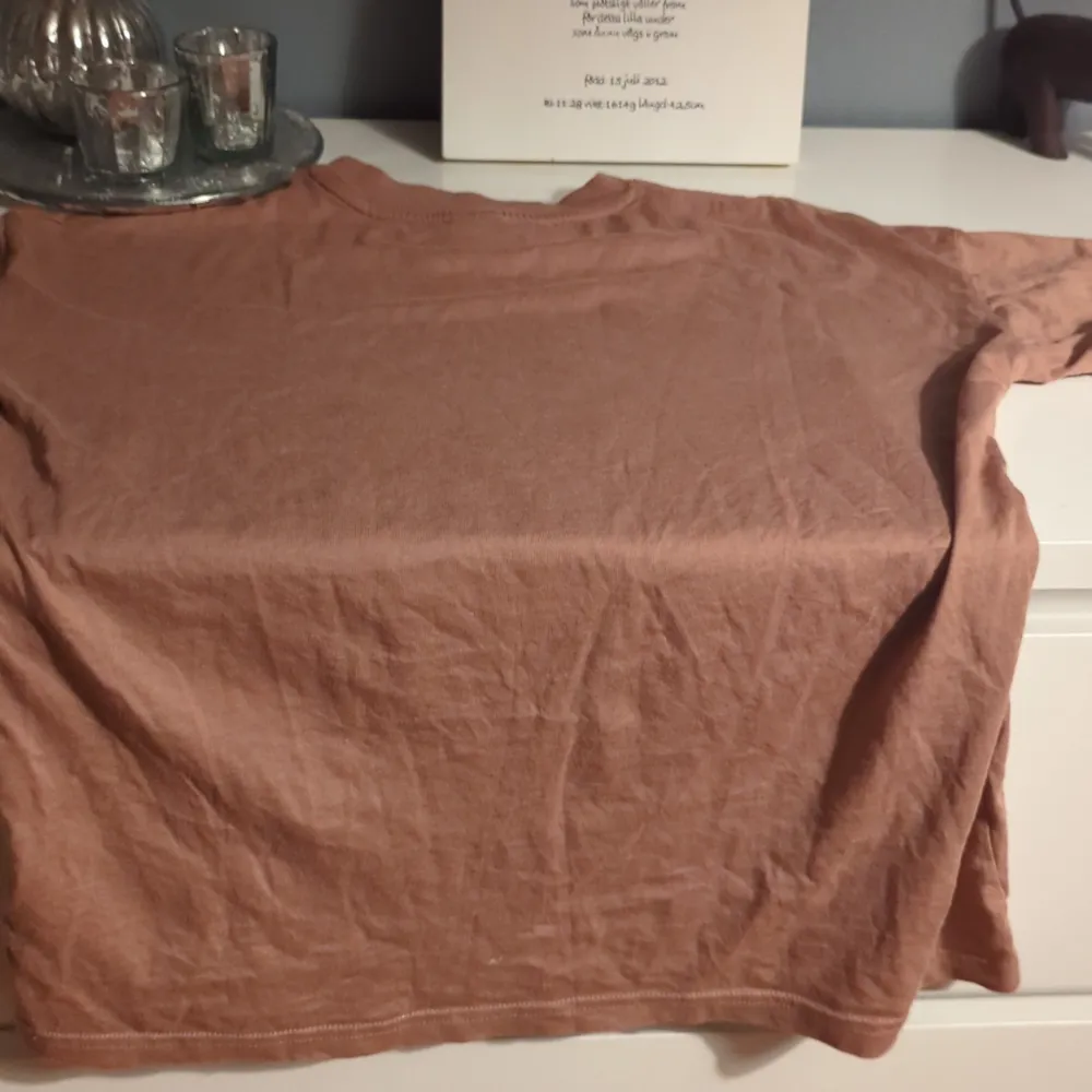 Säljer en brun t-shirt med ett färgglatt tryck på framsidan som säger 'Best Thing Ever'. T-shirten är kortärmad och gjord i ett mjukt material, perfekt för vardagsbruk. Den har en avslappnad passform och är i bra skick.. T-paidat.