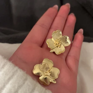Guldblommiga örhängen - Säljer ett par superfina örhängen i form av blommor i guld. De är perfekta för att piffa upp vilken outfit som helst och ger en elegant touch. Passar både till vardags och fest. 🌼