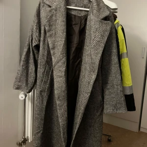 Grå kappa  - Säljer en elegant grå kappa. Den har långa ärmar och ett bälte i midjan för en snygg passform. Perfekt för höst och vinter, och ger en stilren look. Kappan är i mycket bra skick och redo för nya äventyr!