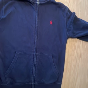 Mörkblå hoodie från Polo Ralph Lauren - Säljer en snygg mörkblå hoodie från Polo Ralph Lauren i storlek L. Den har en dragkedja framtill och en klassisk röd logga på bröstet. Perfekt för höst och vår, med långa ärmar och en skön passform. Perfekt för en grish look! 💙