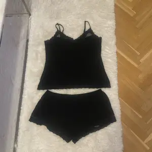 Snyggt svart set från Hunkemöller med ett linne och matchande shorts. Linnet har smala axelband och spetsdetaljer vid halsringningen. Perfekt för en mysig hemmakväll eller som nattplagg. Setet är i mycket bra skick och känns både bekvämt och stilrent. Säljes på grund av fel storlek 