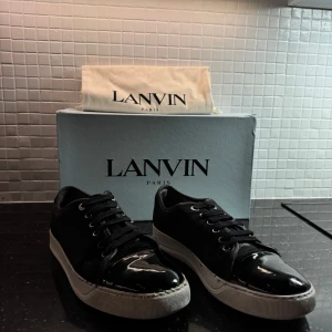 Svarta sneakers från Lanvin - Säljer ett par svarta Lanvin sneakers i bra skick. De har en snygg glansig tå och klassisk snörning. Perfekta för både vardag och fest! Sulan är lite sliten men fortfarande i bra skick. Kommer med originalkartong och dustbag.