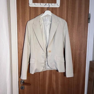 Beige kavaj från MNG Suit - Säljer en stilren beige kavaj från MNG Suit i storlek M. Kavajen har en klassisk design med en knapp framtill och två fickor. Perfekt för både vardag och festliga tillfällen. Passar bra till höst och vår!