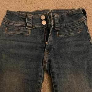 Blå jeans med knappdetaljer - Säljer ett par bootcut jeans från H&M från Barnavdelningen i storlek 140 med knappar där bak. Passar till det mesta!