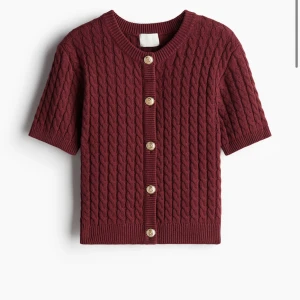 Vinröd kortärmad kofta - Säljer en superfin vinröd kofta med korta ärmar och snygga flätstickade detaljer. Den har knappar fram och är perfekt för både höst och vår. Passar lika bra till jeans som till en kjol. Den är slutsåld på hm hemsidan!!