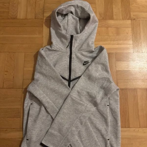 Grå träningsset från Nike - Säljer ett grått träningsset från Nike i mycket bra skick. Setet består av en långärmad hoodie med dragkedja och matchande byxor. Perfekt för träning eller chill. Materialet är mjukt och bekvämt, och det finns praktiska fickor med dragkedjor. Passar perfekt för höst och vår!