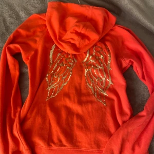 Rosa hoodie från Victoria's Secret - Säljer en supercool rosa hoodie från Victoria's Secret med glittriga vingar på ryggen. Den har en dragkedja framtill och en mysig huva. Perfekt för att liva upp din vardagslook! 🩷