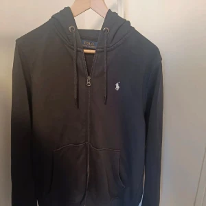 Ralph Lauren Zip - Jag säljer min väldigt snygga och eftertraktade Ralph Lauren zip hoodie. Nypris ligger på ca 1999kr. Den är i färgen svart och storlek M. Den är i väldigt bra skick och har inga som helst slitningar eller defekter. Köpt från Plick 