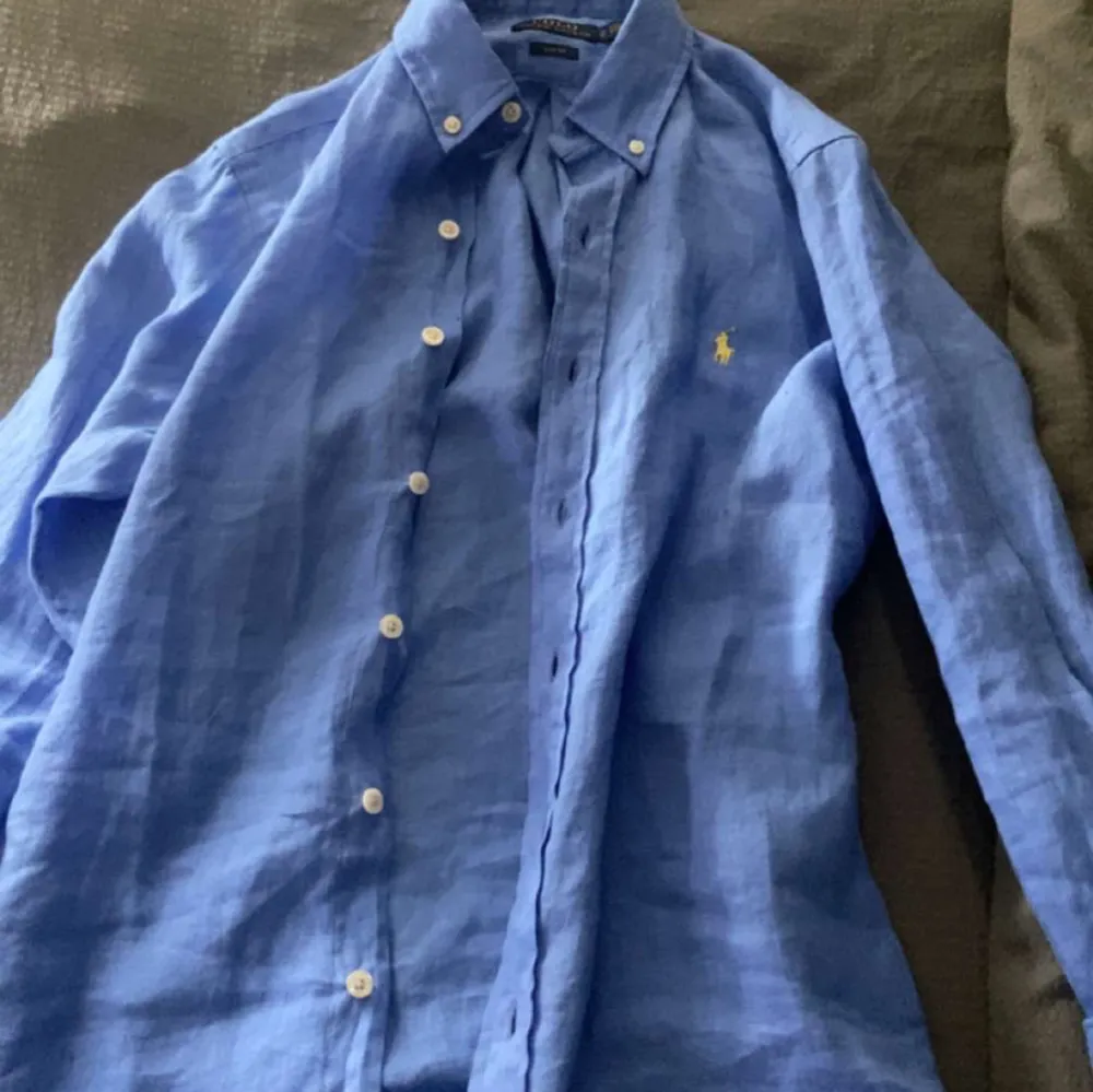 Säljer en snygg blå linneskjorta från Ralph Lauren. Skjortan har långa ärmar och klassiska knappar framtill. Perfekt för både vardag och festliga tillfällen. Den är i mycket bra skick och har en liten broderad logga på bröstet. Vid mer funderingar bara att höra av er!! ✅. Skjortor.