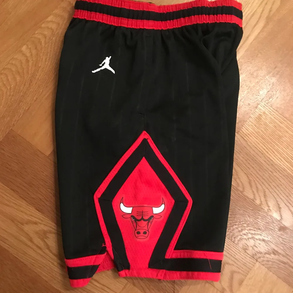 Säljer ett par svarta basketshorts från Jordan med röda detaljer och Chicago Bulls-logga. Shortsen har en elastisk midja. För barn.. Shorts.