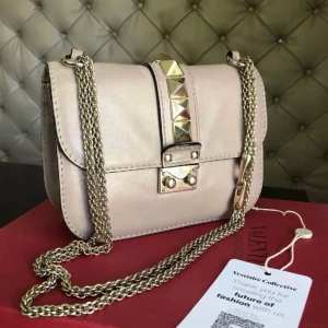 Beige/rosa valentino väska - Säljer min supersnygga beigea axelväska i skinn med guldfärgade kedjor och nitar från valentino (äkta). Väskan har en stilren design med en dekorativ rem och spänne framtill. Nypris på denna väska ca: 20 000. Köpt från Vestiaire❤️kan skicka fler bilder om man vill ha, samt diskutera pris då tecken på användning finns!
