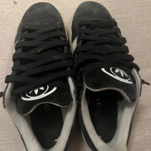 Svarta Adidas Campus sneakers - Säljer ett par svarta Adidas Campus sneakers i bra skick. De har den klassiska tre-randiga designen i vitt på sidorna och en bekväm passform. Perfekta för vardagsbruk och streetwear-stil. Lite slitna sulor men fortfarande mycket användbara.