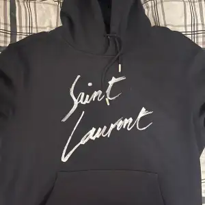 Säljer en snygg svart hoodie från Saint Laurent med deras ikoniska logga i vitt på framsidan. Den är i storlek M, men sitter mer som en S. Skick 9/10 då den är välvårdad och skonsamt använd. Vid frågor är det bara att skriva!