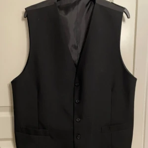 Svart väst XXL (Sergio Rossi) - Säljer denna lyxiga väst i både matt och “glans” svart tyg. Västen är använd en gång och är helt ny i skick. Den har stl XXL och är köpt från Sergio Rossi.