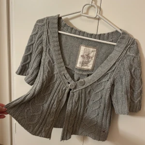 Grå stickad bolero från Hollister - Säljer en superfin grå stickad bolero från Hollister i storlek S. Den har korta ärmar och två stora knappar framtill. Perfekt för höst och vår när du vill ha något mysigt men ändå stilrent. Boleron har ett snyggt flätmönster och är i mycket bra skick. Passar perfekt till både jeans och kjol!