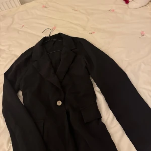 Svart kavaj med knapp - Elegant svart kavaj med en enkel knapp framtill. Perfekt för en stilren look. Kavajen har klassiska slag och är designad för en tidlös stil.