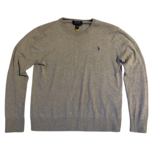 Grå tröja från Polo Ralph Lauren - Säljer en stilren grå tröja från Polo Ralph Lauren med det klassiska broderade logotypen på bröstet. Tröjan har långa ärmar och ribbade muddar vid ärmslut och nederkant. Perfekt för en avslappnad och snygg look.