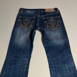 Lågmidjade jeans  - Snygga blå bootcut jeans med unikt broderi på bakfickorna. Perfekt för en avslappnad stil med en touch av detaljer. Klassisk femficksdesign och bekväm passform. Midja=37cm  Innerbenslängd=76cm  grenmått=20cm