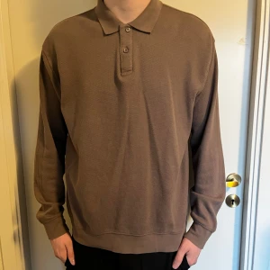 Brun pikétröja med långa ärmar - Säljer en stilren brun pikétröja med långa ärmar. Tröjan har en klassisk krage och knappar framtill. Perfekt för en avslappnad men ändå uppklädd look.