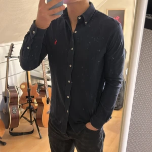 Mörkblå skjorta från Ralph Lauren - Snygg mörkblå skjorta från Ralph Lauren med klassisk krage och knappar framtill. Den har en röd broderad logotyp på bröstet som ger en stilren touch. Perfekt för en elegant look.