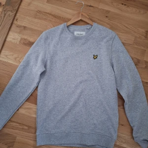 Grå sweatshirt från Lyle & Scott - Säljer en stilren grå sweatshirt från Lyle & Scott med rund hals och ett litet broderat emblem på bröstet. Tröjan är tillverkad i ekologiskt material och har långa ärmar. Perfekt för en avslappnad look. Den här tröjan är helt nytt, Säljs pga den är för liten för mig helt enkelt och har suttit i garderoben. Priset kan alltid diskuteras!