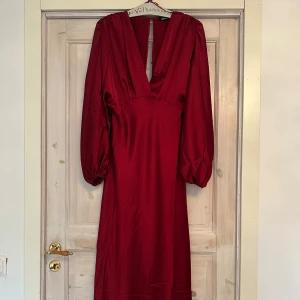 Vinröd klänning från Gina Tricot - Elegant vinröd klänning från Gina Tricot med långa ärmar och v-ringad design. Perfekt för festliga tillfällen i den stilrena look. Helt slutsålt på hemsidan, endast använt en gång. Storlek 36.