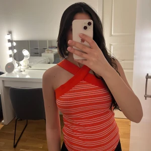 Röd och vit randig bodysuit - Säljer en snygg röd och vit randig bodysuit med korsade axelband. Perfekt för en somrig look. Den har en åtsittande passform och är tillverkad i ett mjukt material.