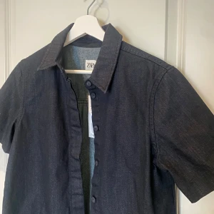 Svart kortärmad skjorta från Zara - Snygg mörkblå kortärmad skjorta från Zara i jeansmaterial. Skjortan är helt oanvänd, prislappen är kvar.  Ny pris 559, jag säljer den för 150 kr!