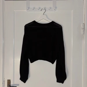 Svart stickad tröja - Säljer en svart stickad tröja med lång ärm och en croppad design. Perfekt för kyligare dagar och kan enkelt matchas med olika outfits.