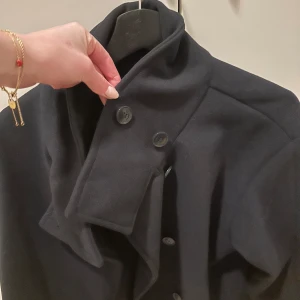 Svart kappa med knappar - Elegant blå kort  kappa med hög krage och knappar framtill. Perfekt för kyligare dagar med sin stilrena design och klassiska look.