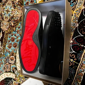 Louboutin skor - Snygga svarta sneakers med nitar på tån och sidorna. Skorna har en röd sula och snörning framtill. Perfekta för att ge en edgy touch till din outfit.