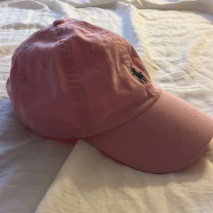 Rosa keps från Polo Ralph Lauren - Snygg rosa keps från Polo Ralph Lauren med broderad logga framtill. Kepsen har en justerbar rem baktill för perfekt passform. 