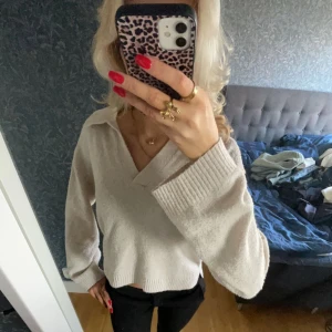 Beige stickad tröja med krage - Säljer en stilren beige stickad tröja med krage och långa ärmar. Tröjan har en avslappnad passform och ribbade muddar vid ärmslut. Perfekt för en mysig och trendig look. Lite nopprig men inget man tänker på.