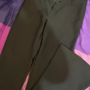 Svarta byxor från Gina Tricot - Snygga svarta byxor från Gina Tricot i storlek XS. Byxorna har en stilren design med knappar och dragkedja framtill samt fickor med knappar bak. Perfekta för en chic look. DRAGKEDJAN ÄR SÖNDER men man kan fixa det på nåt sätt.💕