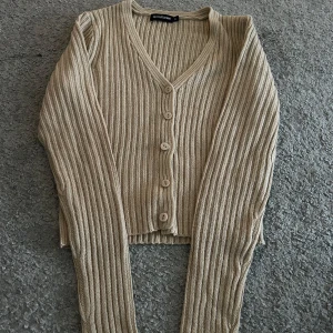 Beige ribbad kofta från Pretty little things - Säljer en snygg beige ribbad kofta. Den har en v-ringning och knappar framtill. Perfekt för lager-på-lager och att hålla sig varm under kyligare dagar.