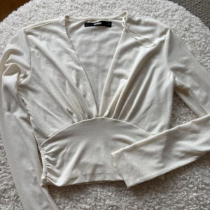 Vit v-ringad topp från BikBok - Säljer en stilren vit v-ringad topp från BikBok i storlek XS. Toppen har långa ärmar och en elegant passform som framhäver midjan. Perfekt för att skapa en chic look.